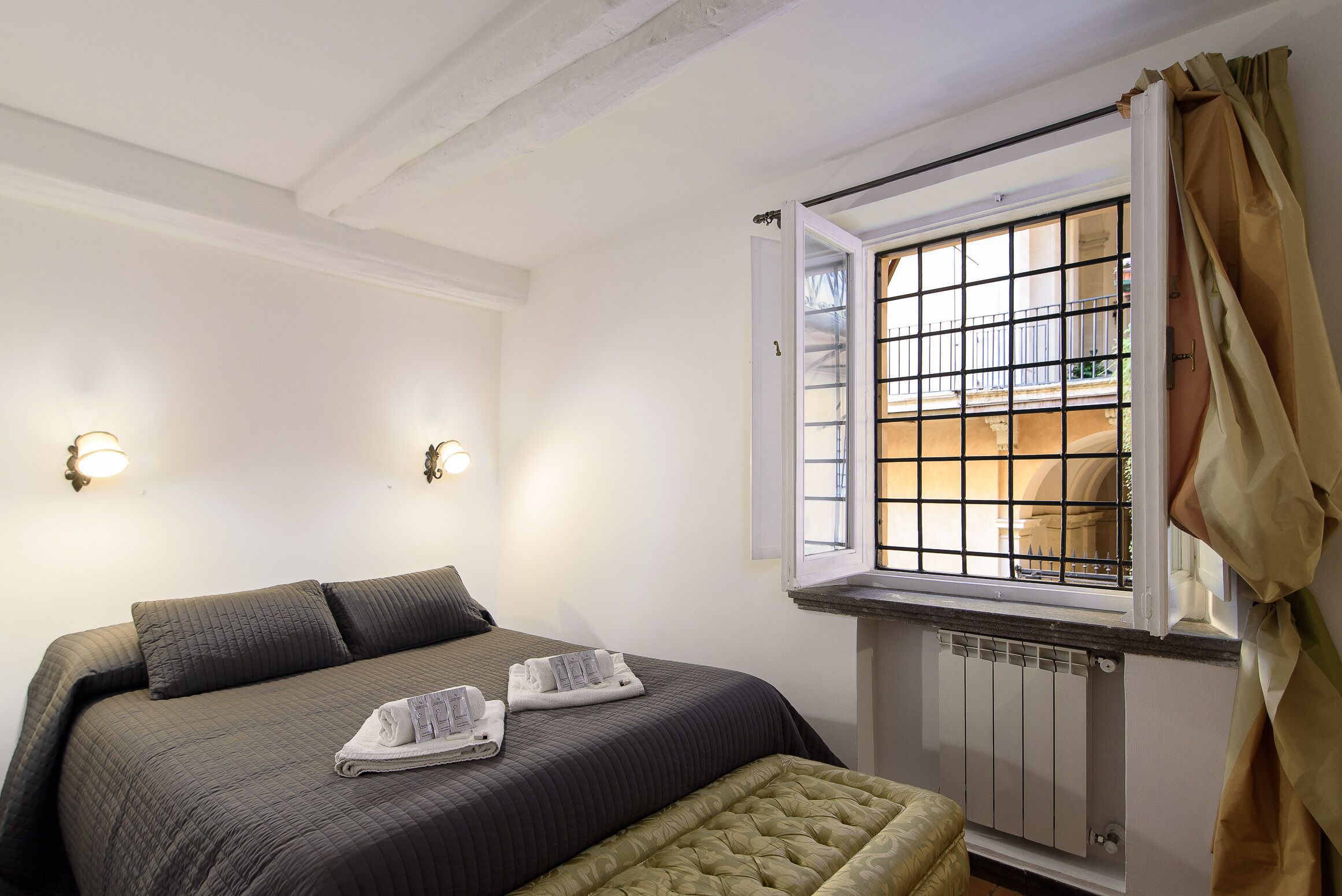 A hotel room with a bed, two wall-mounted lights, a window with a view, and a radiator.