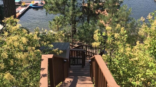 Una terraza de madera que conduce a un muelle con barcos, rodeada de árboles frondosos y un lago.