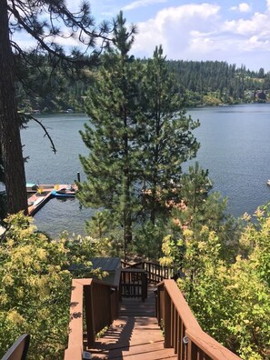 Eine Holzterrasse führt zu einem Steg mit Booten, umgeben von dichten Bäumen und einem See.