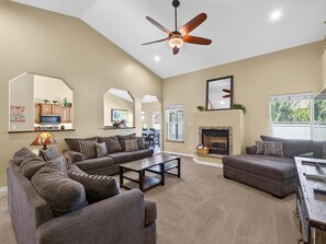 A spacious living room with a ceiling fan, a fireplace, and a dining area visible through an archway.