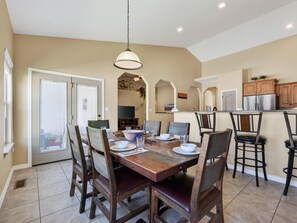 A dining area with a wooden table, chairs, and a hanging light fixture. - Velo III: BBQ, Fire Pit & Dog-Friendly Retreat (Fruita)