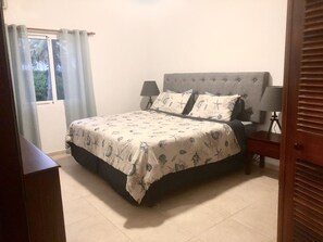 Um quarto com uma cama, duas luminárias de cabeceira, uma janela com cortinas e vista para árvores.