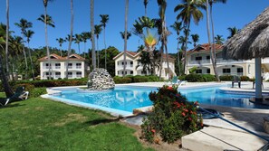 Resort com piscina, palmeiras e uma construção de colmo.