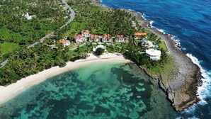Vista aerea di una proprietà costiera con spiaggia, acque cristalline e una strada che conduce alle case.