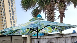A patio with a table and chairs, a wooden fence, and a palm tree. - White Sandy Beaches, Gulf Front Complex, Heated Pool, Private Patio (Navarre)