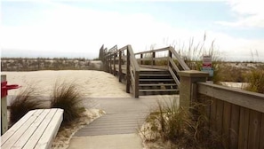 A wooden boardwalk leading to a beach with a staircase and a sign.