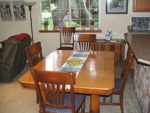 Un comedor con una mesa de madera, sillas y una ventana que da a vista de árboles y un edificio.