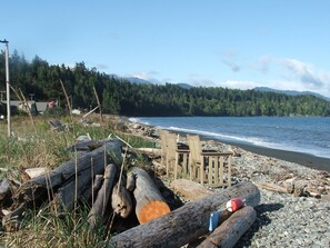 A beach with logs, a wooden structure, and a forested mountain backdrop.