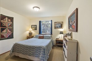 Un dormitorio con cama, mesita de noche, lámpara, estantería y ventana con cortinas.