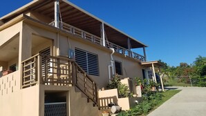 Una casa de dos pisos con balcón, escalera y entrada protegida por una reja.