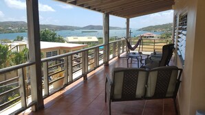 Un balcón techado con vistas al agua, una hamaca y mobiliario de exterior.