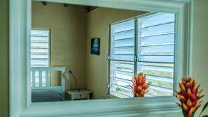 Un dormitorio con cama, mesita de noche, lámpara y una ventana con contraventanas.