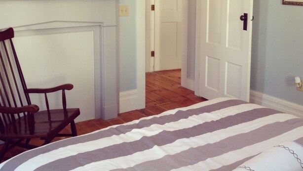 A bedroom with a bed, a chair, a fireplace, and a door leading to another room.