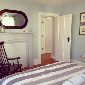 A bedroom with a bed, a chair, a fireplace, and a door leading to another room.