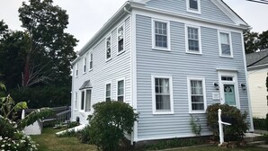 A two-story house with a gabled roof, white siding, and multiple windows.