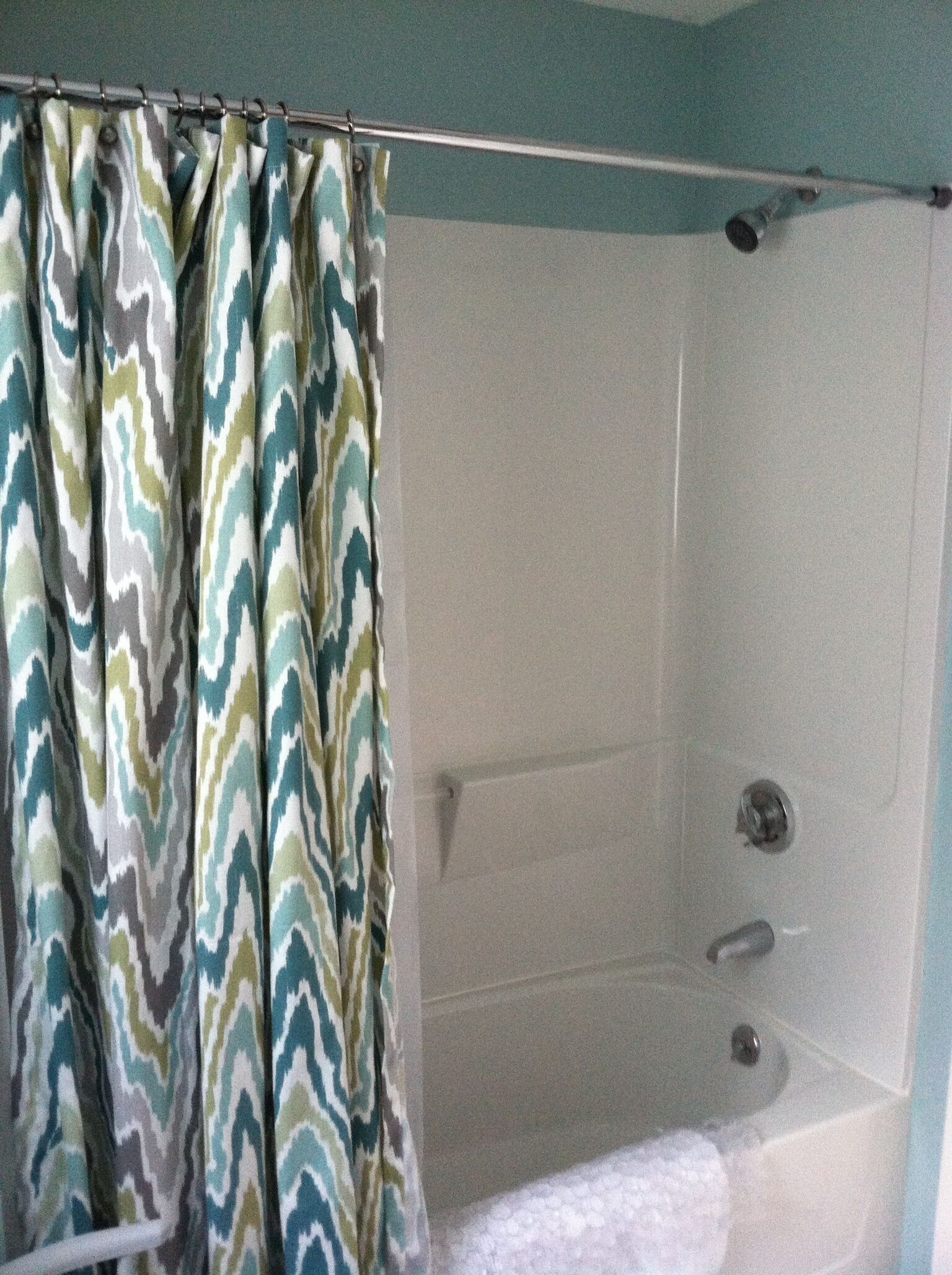 A shower area with a patterned curtain, a bathtub, and a tiled wall.