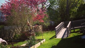 A garden with a wooden deck, a stone wall, and a pink flowering tree.