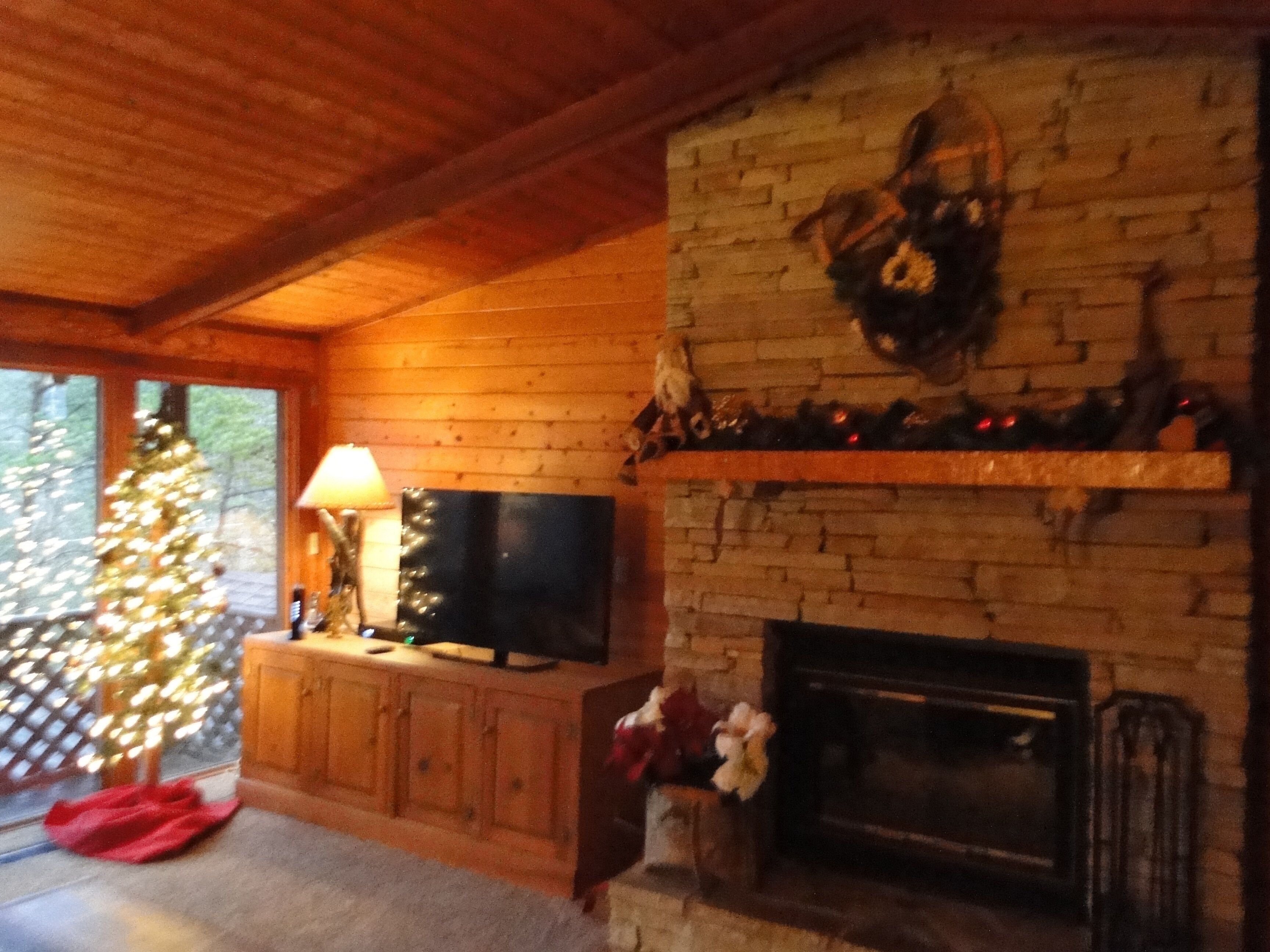 A cozy living room with a fireplace, a television on a wooden cabinet, and a Christmas tree.