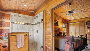 Ein Holzblockhaus-Interieur mit Dusche, einem Bett mit kariertem Überwurf und einer Holzkammer mit einer herzförmigen Schublade.