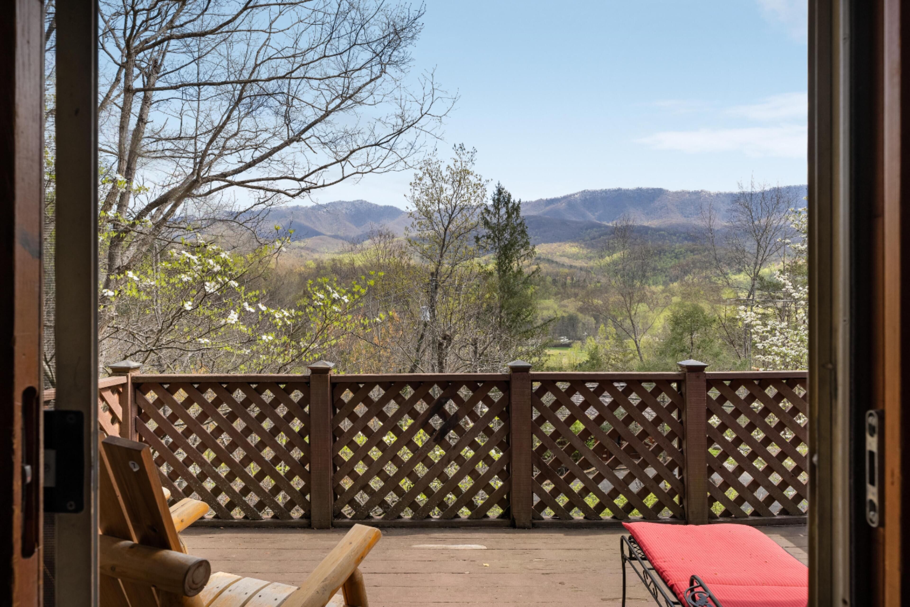 A balcony with a wooden deck, a red cushioned bench, and a metal bed with a red cover.