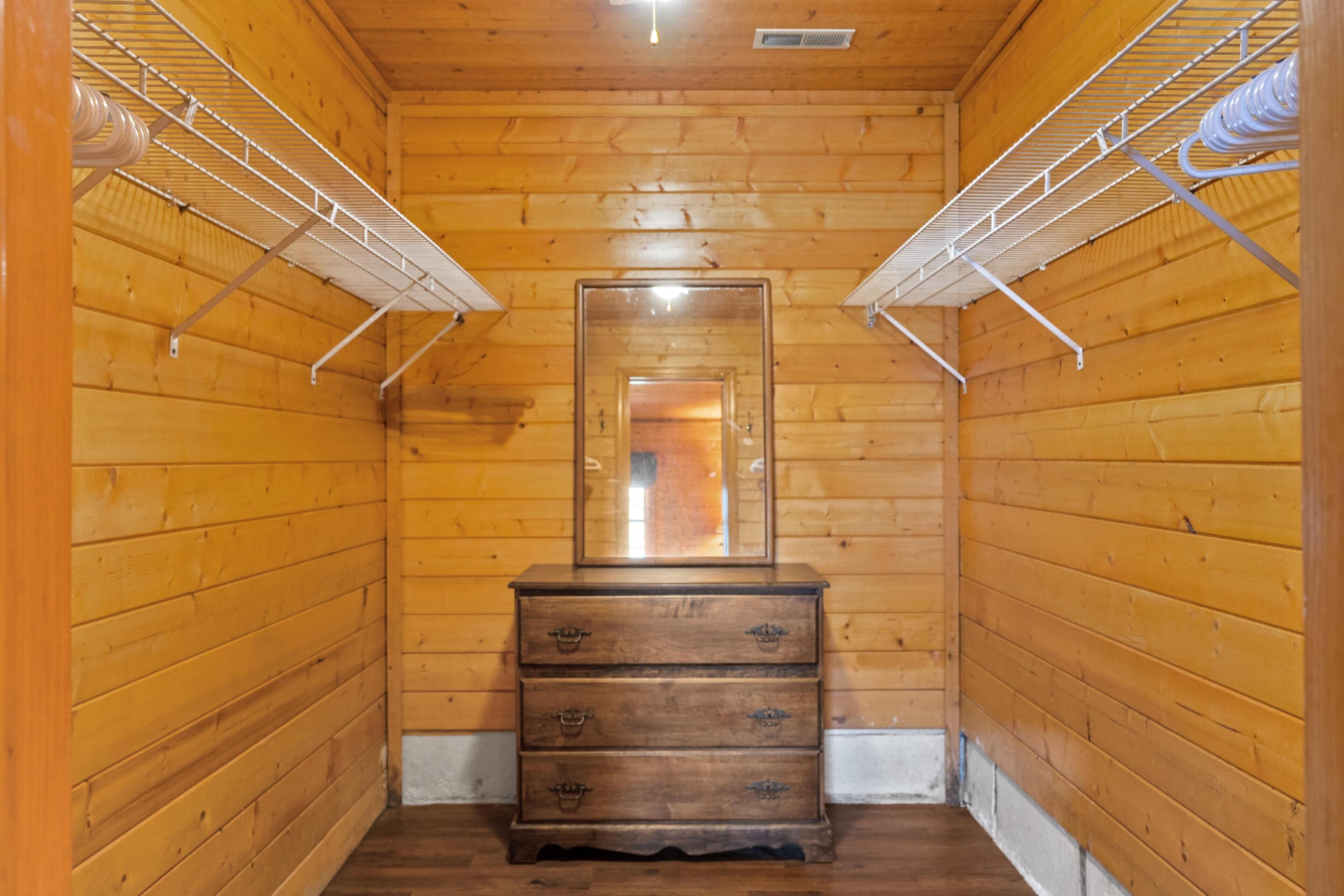 A narrow hallway with wooden walls, a central wooden dresser with drawers, and metal shelving units on either side.