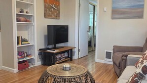 Ein Wohnzimmer mit einem runden Korbtisch, einem Fernseher auf einem Holzständer, einem Bücherregal und einem Sofa.