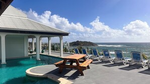 A pool area with lounge chairs and a wooden table, overlooking the ocean. - FantaSea beachfront, every bedroom facing ocean! Remodeled 2024 (Upper Prince's Quarter)