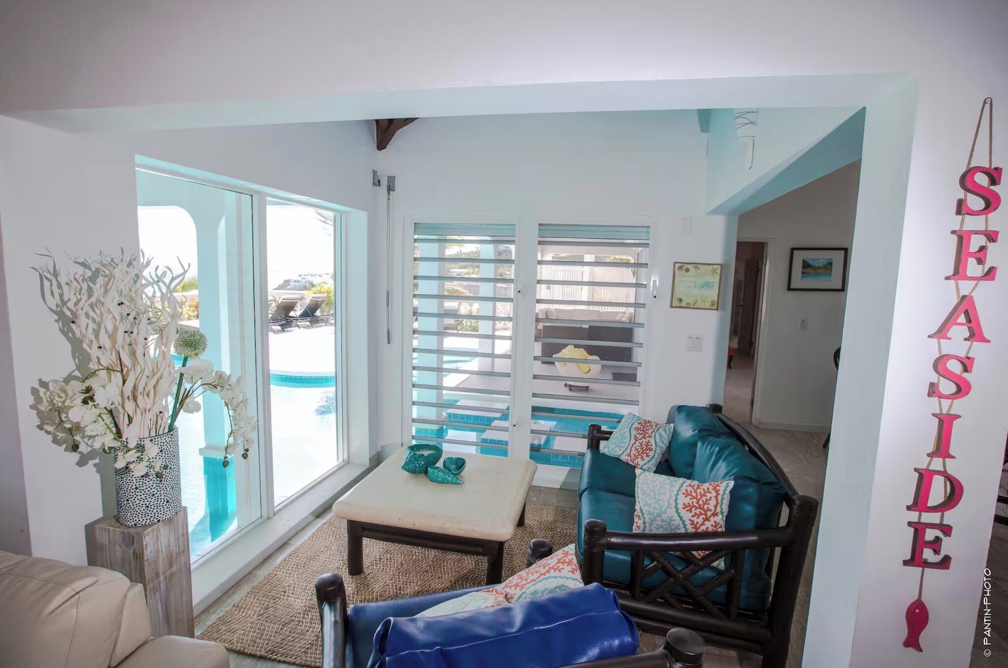 A room with a view of the pool, a teal sofa, a wooden coffee table, and a decorative vase with white flowers.