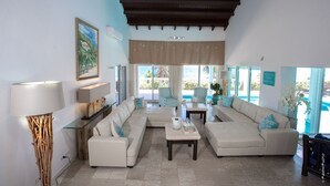 A spacious living room with a large sectional sofa, a coffee table, and a floor lamp. There are two armchairs and a dining table with chairs. The room has large windows with a view of the ocean. - FantaSea beachfront, every bedroom facing ocean! Remodeled 2024 (Upper Prince's Quarter)