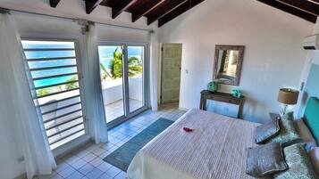 A bedroom with a bed, a nightstand, a mirror, and a view of the ocean through a sliding door.