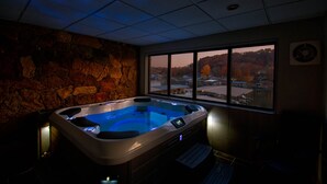 A hot tub in a room with a stone wall and a view of a lake and buildings during sunset. - Spacious Condo with in condo private Hot Tub (Osage Beach)