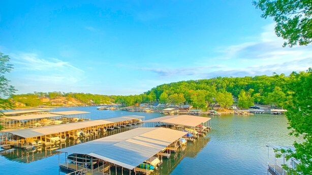 A waterfront property with multiple docked boats, a pier, and a forested hillside in the background. - Spacious Condo with in condo private Hot Tub (Osage Beach)