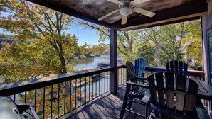 A covered porch with a view of a lake and autumn trees. - Spacious Condo with in condo private Hot Tub (Osage Beach)