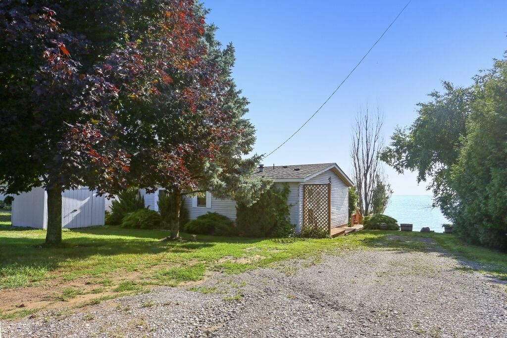 Une petite maison avec une allée en gravier, une clôture en bois et une vue sur l’eau.