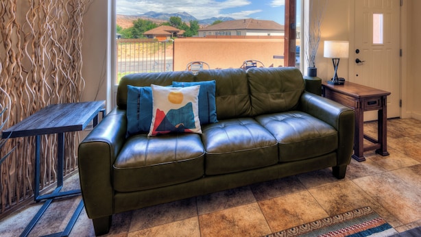 A living room with a green leather sofa, a wooden coffee table, a lamp, and a view of mountains through a large window.