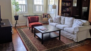 A living room with a white sofa, a red chair, a coffee table, a bookshelf, and a potted plant. - Spacious Sebastopol Home — 5-Minute Walk to Town, Wine Country at Your Doorstep (Sebastopol)
