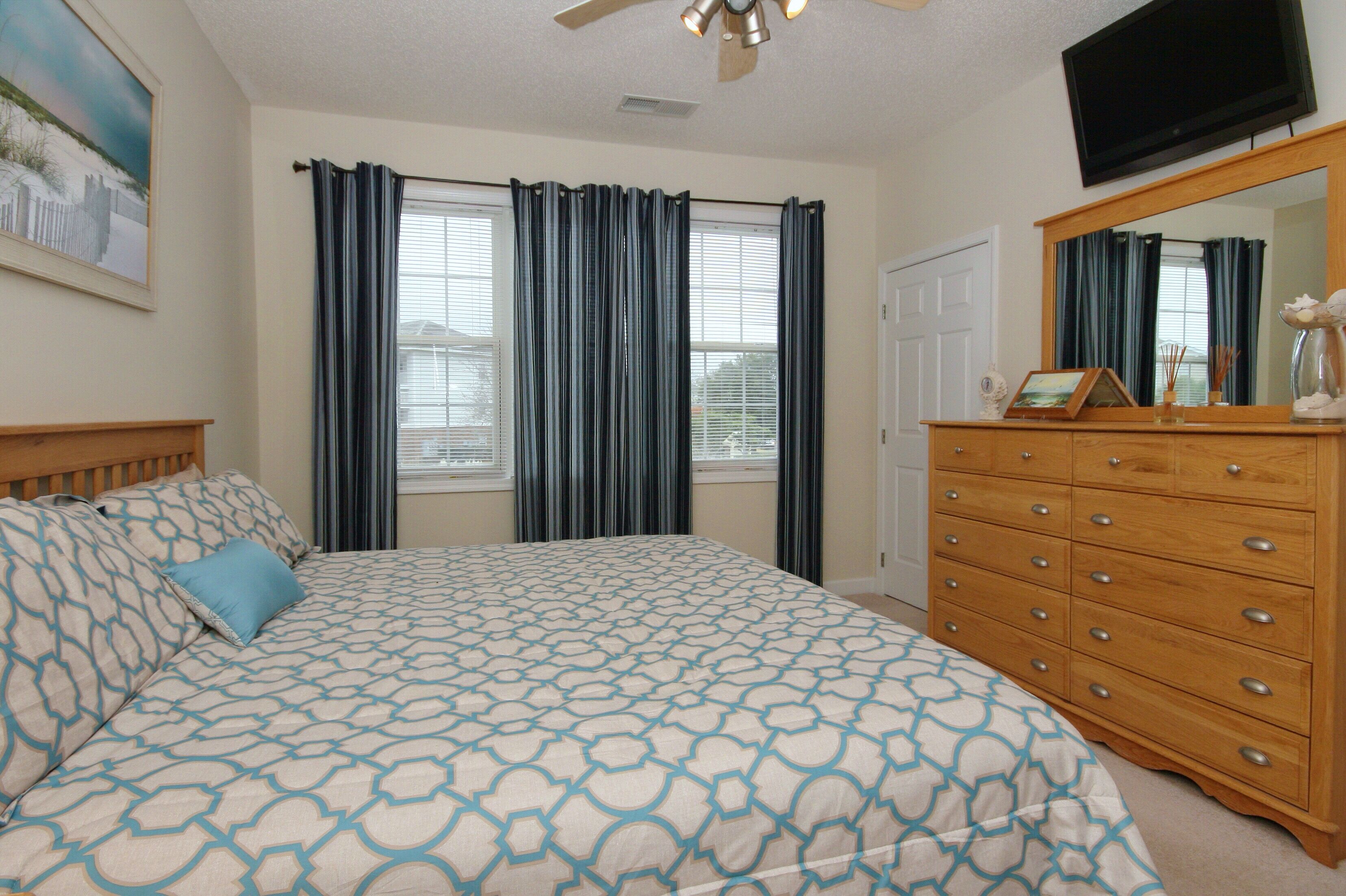 A bedroom with a bed, a dresser, a television, and a window with curtains.