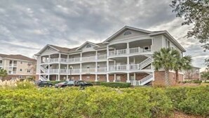 Un hotel de varios pisos con balcones, estacionamiento techado y un césped bien cuidado.