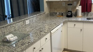Una cocina con gabinetes blancos, encimeras de granito, una licuadora y un escurreplatos.