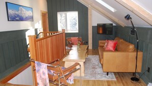 A cozy loft-style living space with a wooden staircase, a brown leather sofa, a dining table, and a TV mounted on the wall. - Revelation Valley Carriage House near Jasper National Park (Valemount)