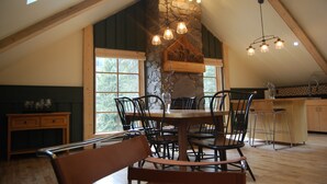 A dining area with a stone fireplace, wooden ceiling beams, and a large window. - Revelation Valley Carriage House near Jasper National Park (Valemount)