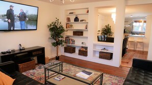 A modern living room with a flat-screen TV, a black sofa, a coffee table, and a bookshelf filled with books and decorative items.