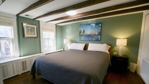 A bedroom with a large bed, two bedside tables with lamps, a window with shutters, a radiator, and a painting on the wall.