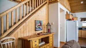 Eine Holztreppe führt zu einem Schlafzimmer im Zwischengeschoss mit rustikalem Dekor, darunter eine Holzkommode und ein Hirschgemälde.