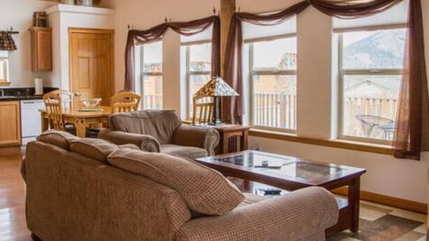 Ein geräumiges Wohnzimmer mit hoher Decke, Holzbalken, einem großen Sofa, einem Couchtisch und Bergblick durch große Fenster.