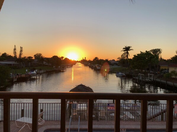 Una vista al atardecer sobre una vía fluvial tranquila con muelles y barcos, una estación de salvavidas y una zona de piscina con sillas y mesas.