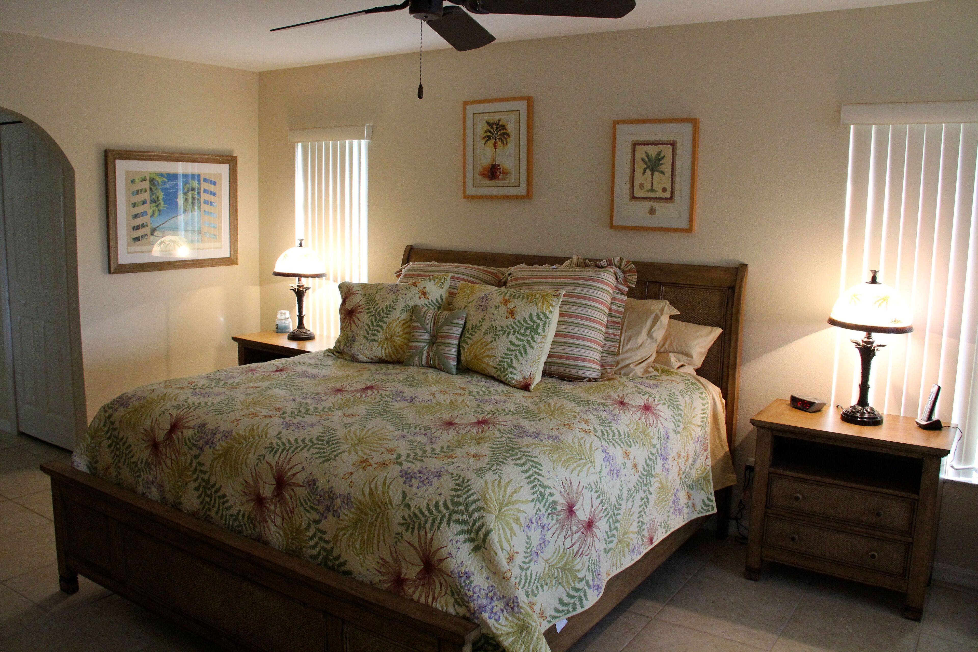 A bedroom with a large bed, two bedside tables, a ceiling fan, and framed pictures on the wall.