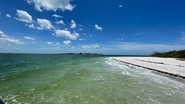 Een helder uitzicht op de oceaan, met een zandstrand en een eiland in de verte.