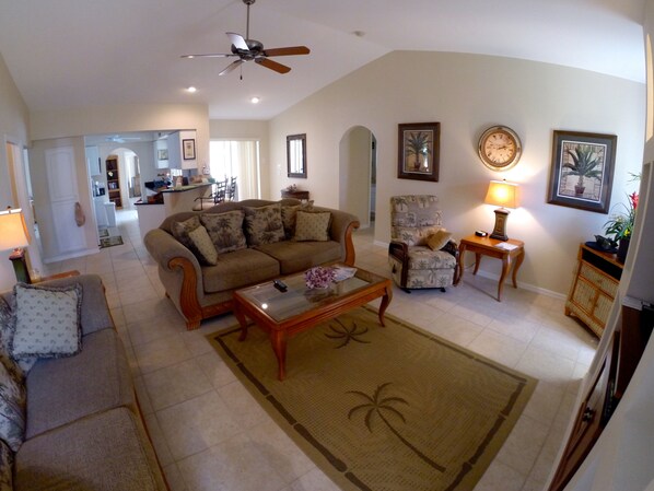 A spacious living room with a large sofa, a coffee table, a patterned armchair, and a dining area in the background.