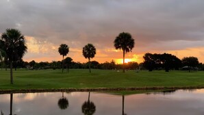 Een golfbaan met een vijver die palmbomen en een ondergaande zon weerspiegelt.